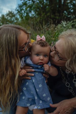 Intimate family portrait with baby in blue dress being embraced outdoors.