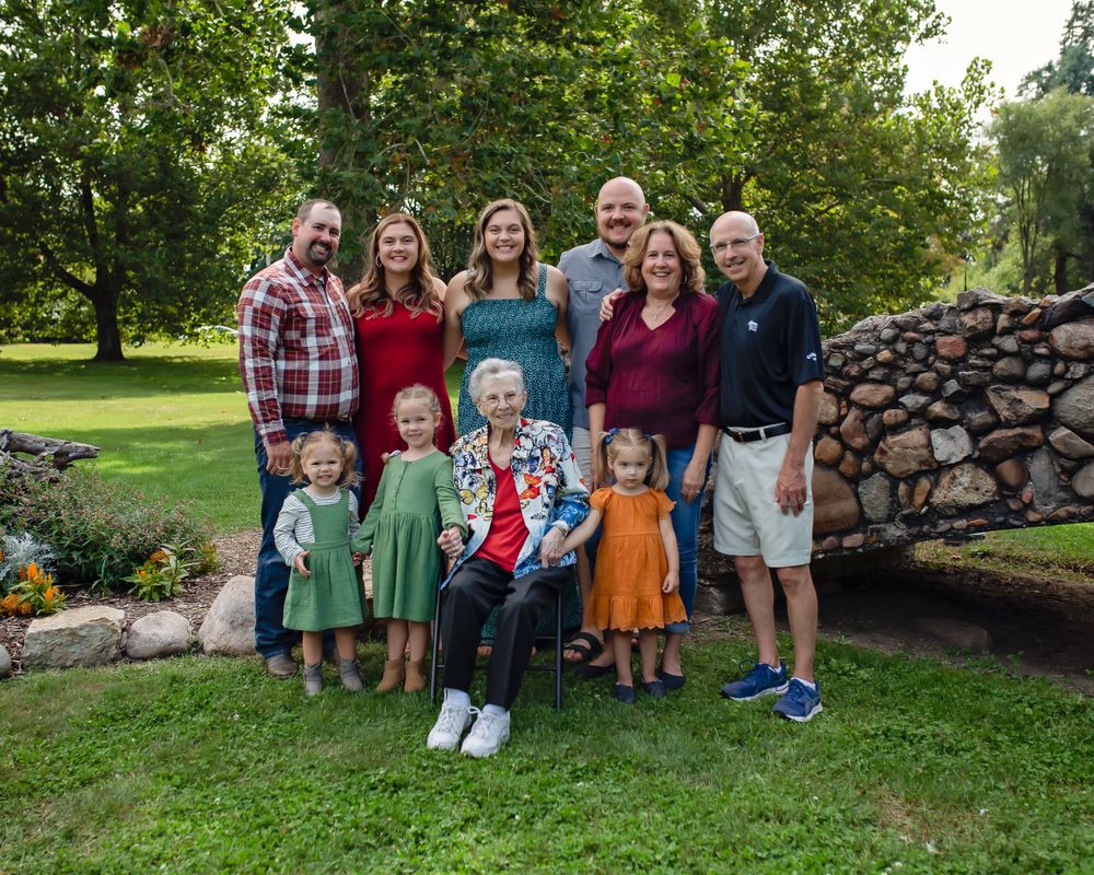 A large group poses together in front of a stone wall in a lush garden setting.