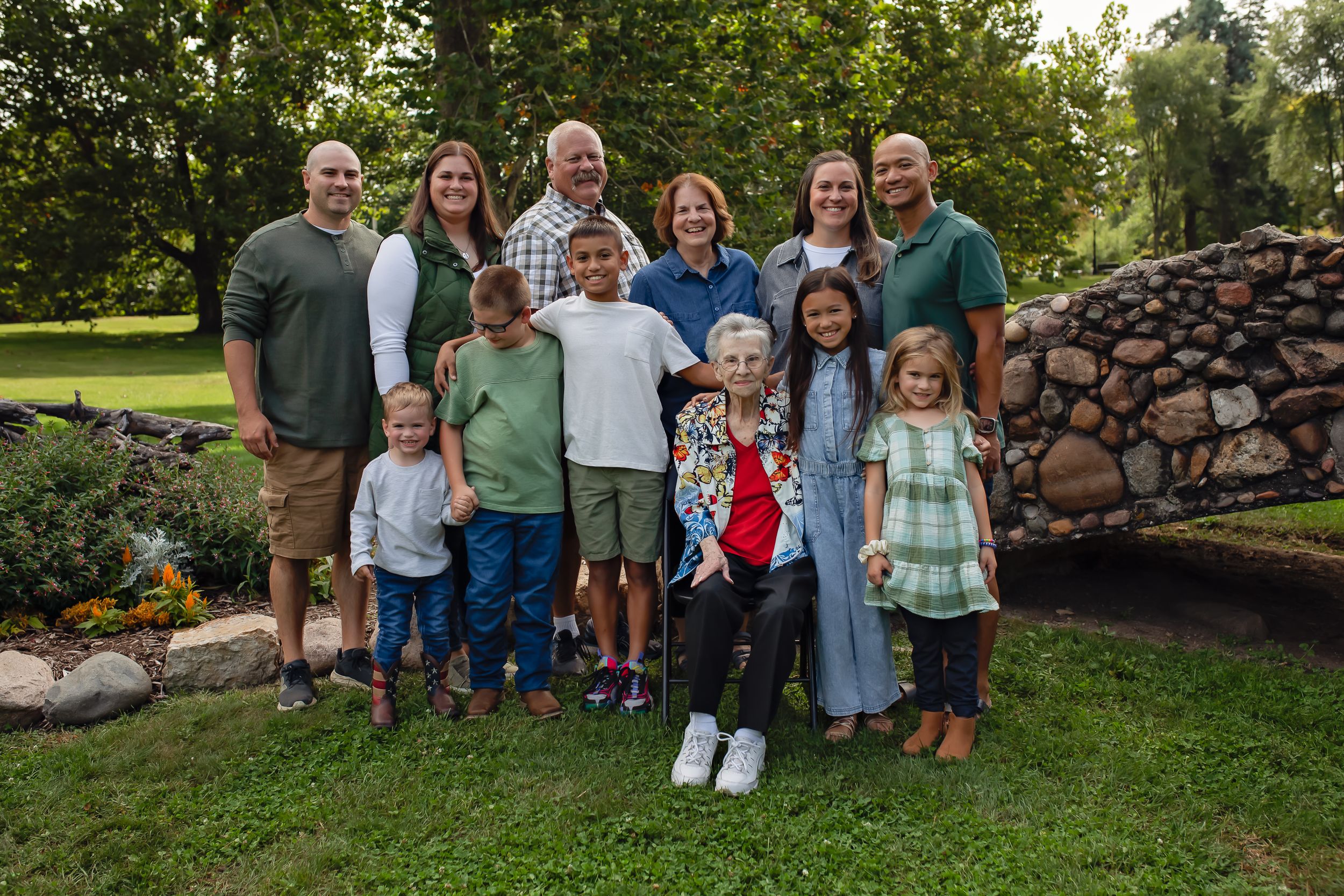 Family gathering outdoors with adults and children standing by a decorative rock wall in a garden.