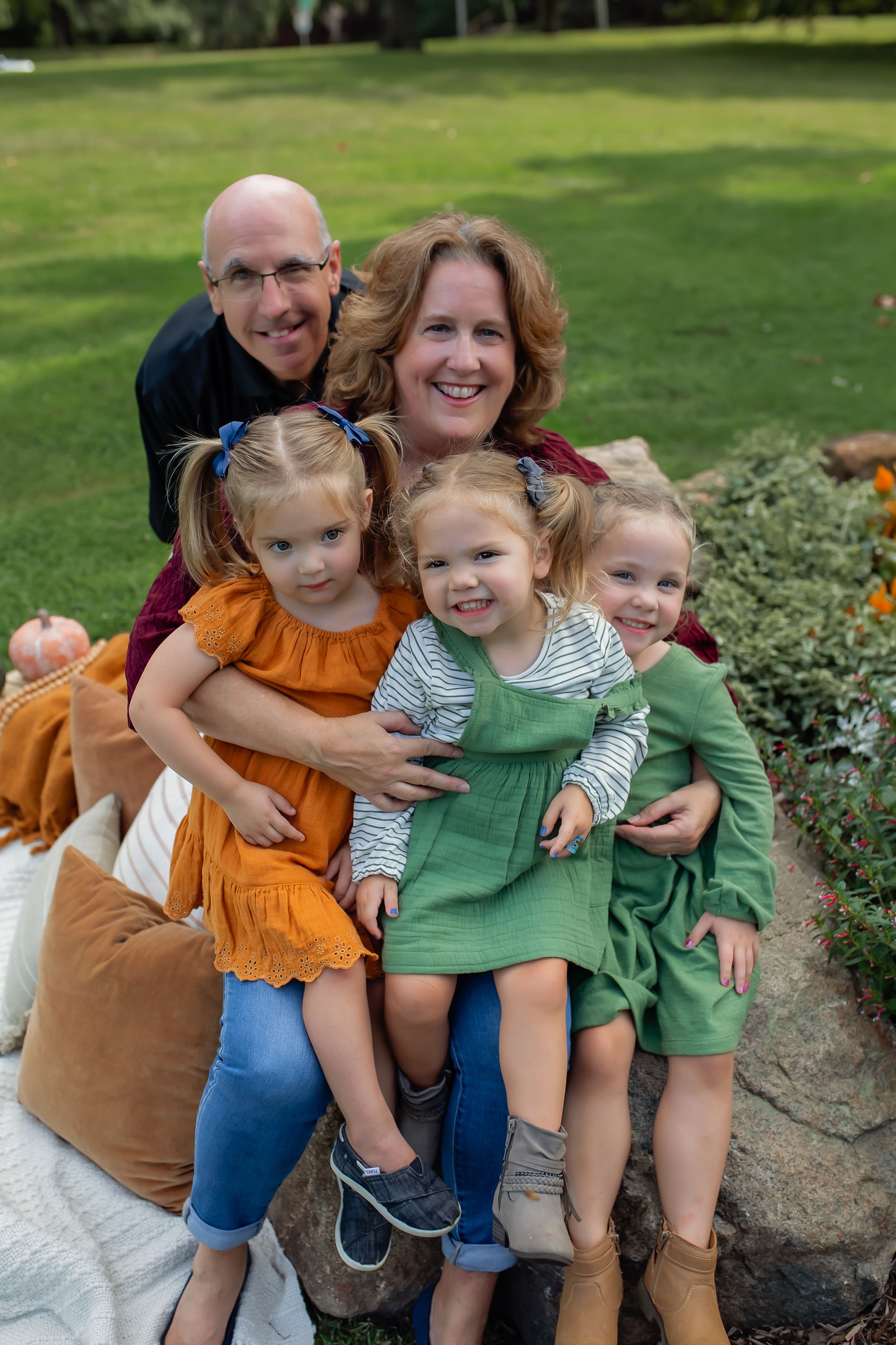 Family members share a joyful moment on garden steps with decorative stone wall backdrop.