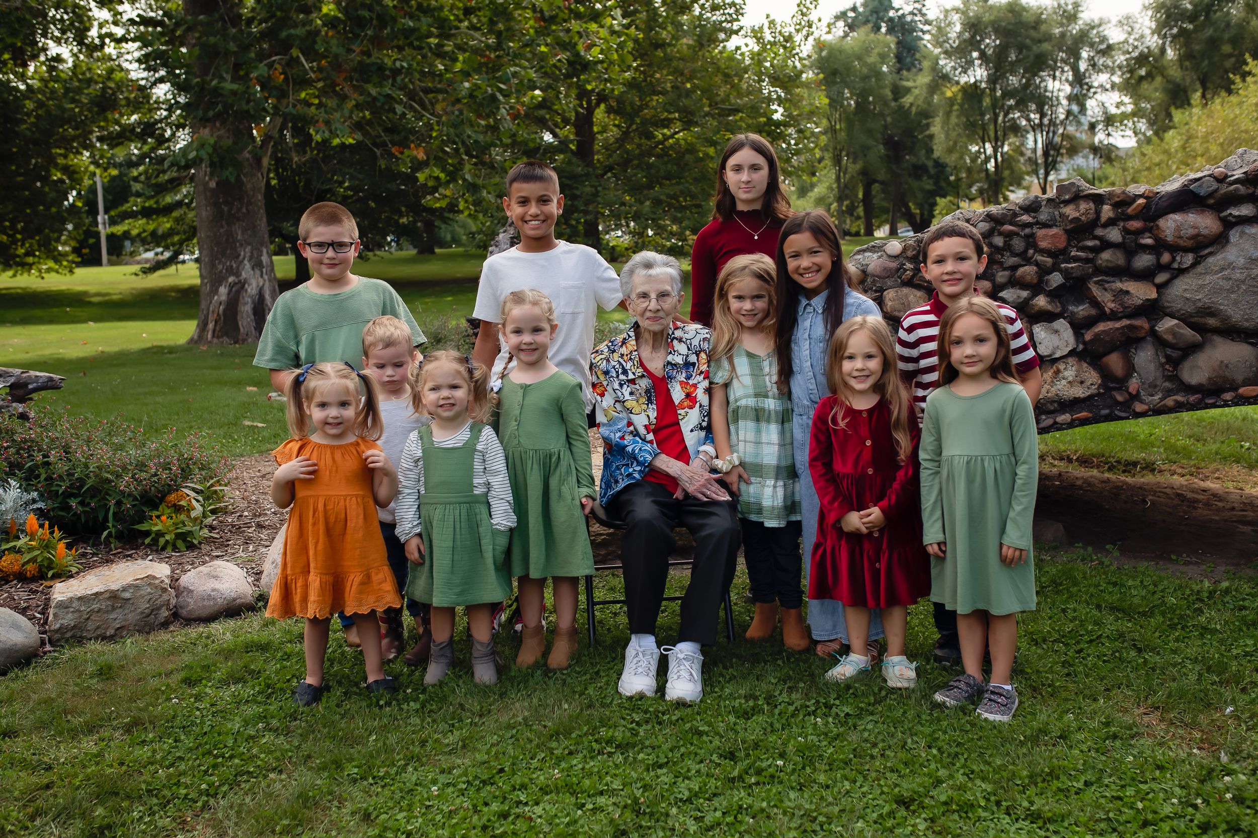 Group photo of children in colorful dresses standing by a rock wall in a garden.