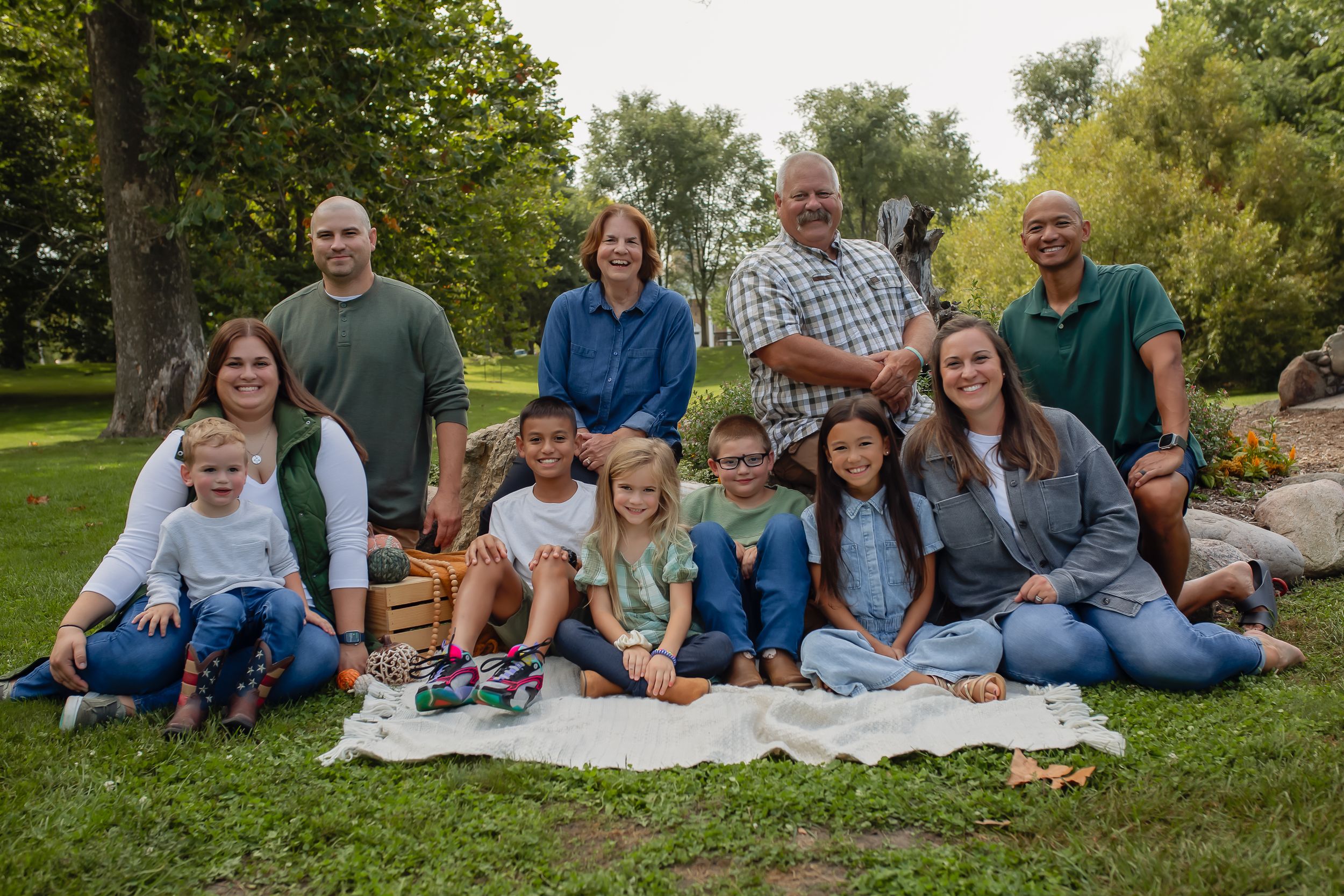 Multi-generational gathering relaxing on a picnic blanket in a green park setting.