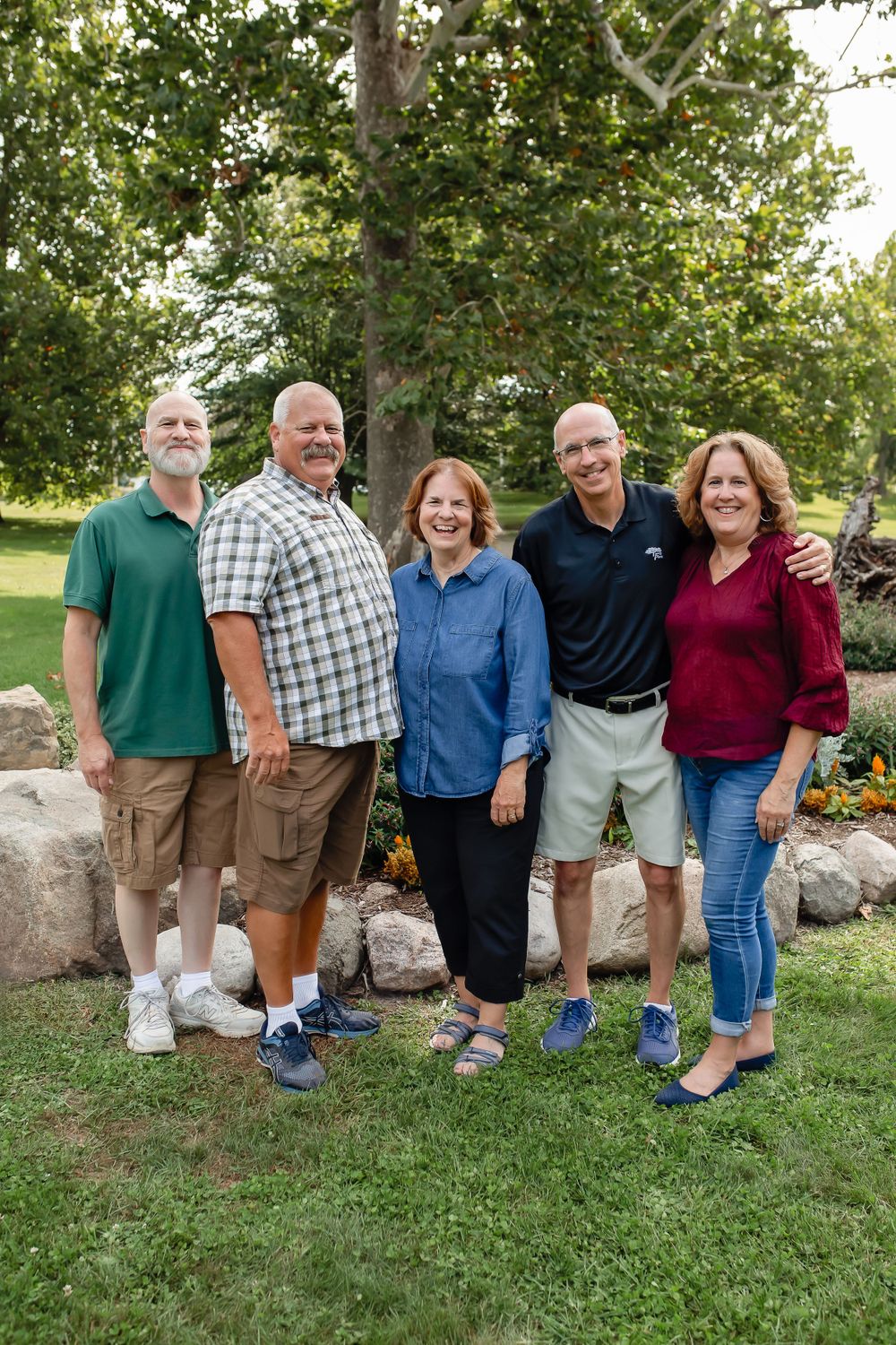 Five adults standing together by a rock wall in a garden setting.