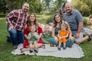 Family group sitting on blanket in garden with stone wall backdrop.