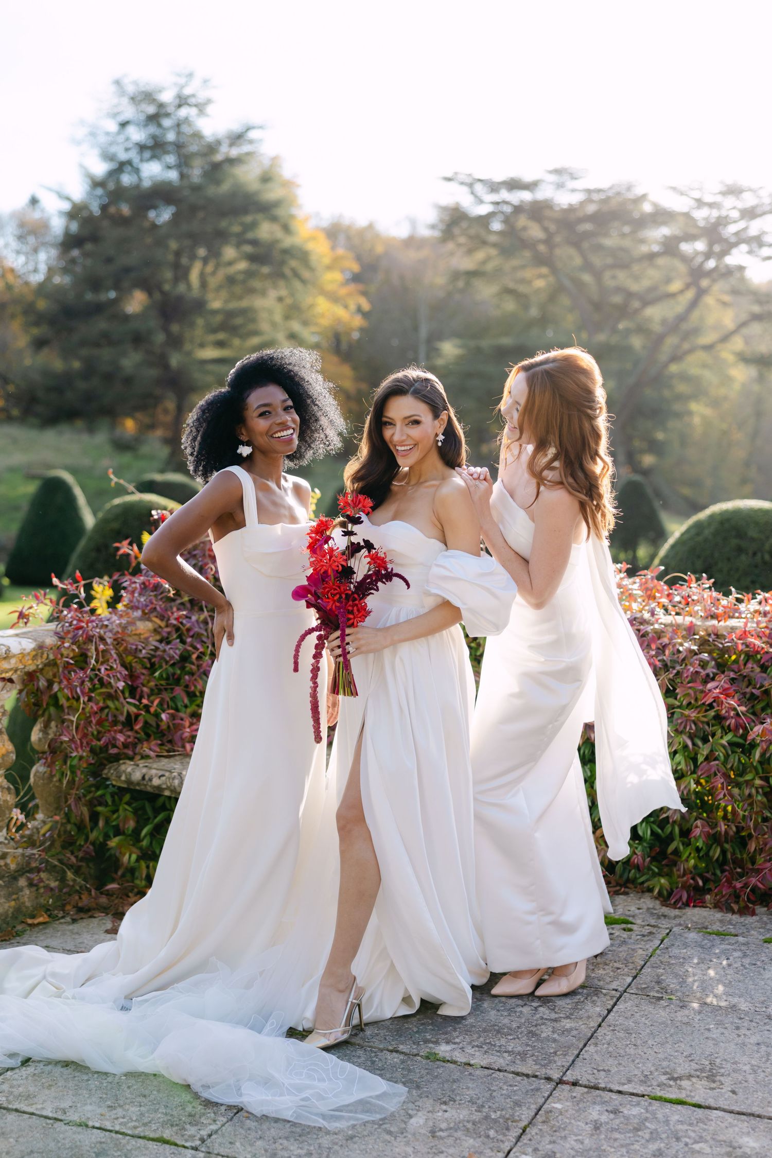 Joyful group in white dresses sitting together among blooming garden flowers.