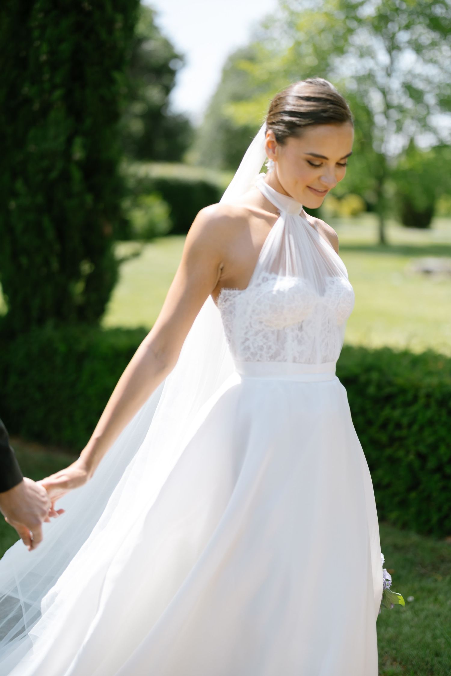 A white wedding dress with lace details flows in the sunlight against a garden backdrop.