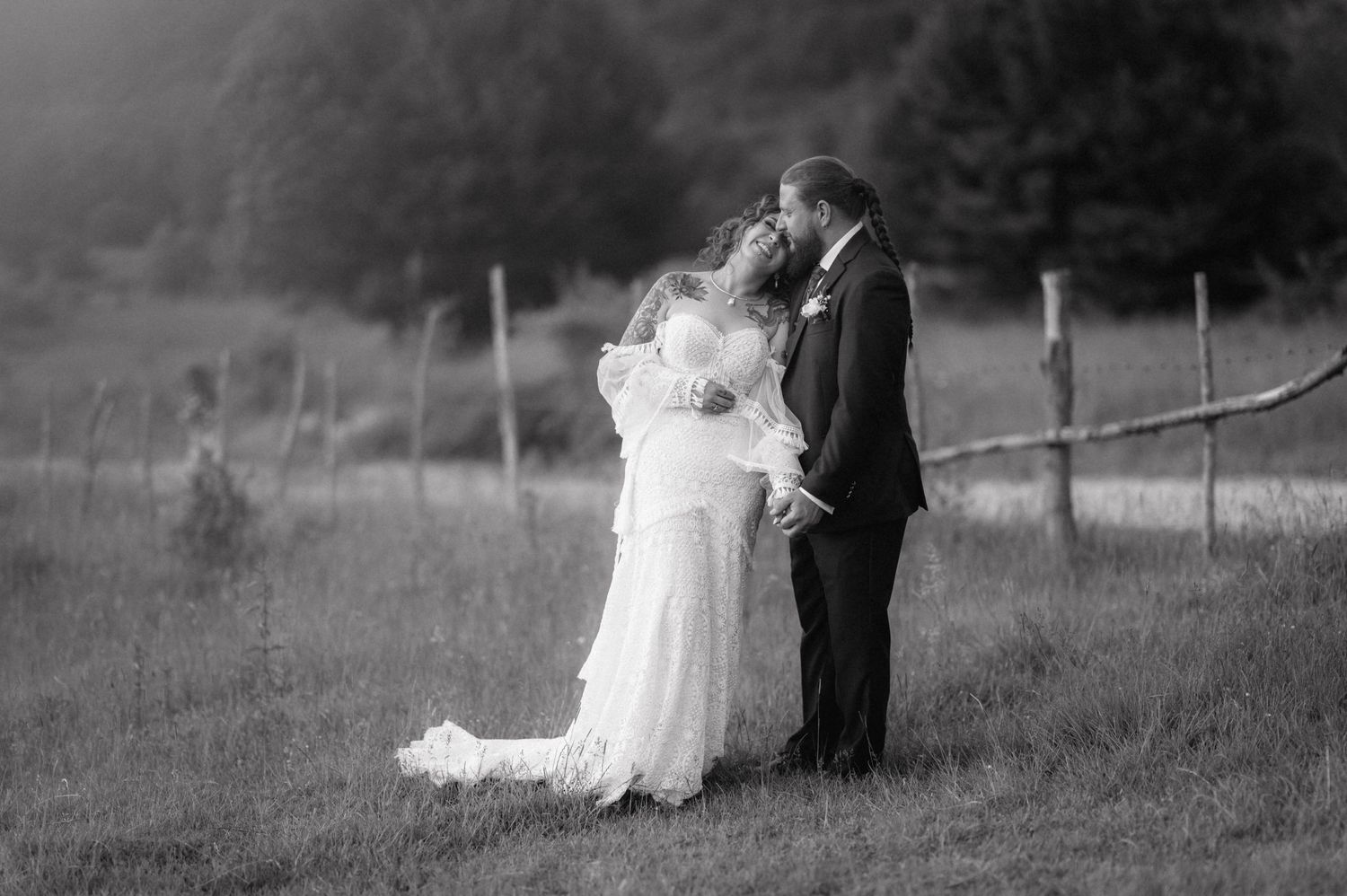 A romantic black and white portrait of a bride and groom embracing in a misty countryside field with a rustic fence.