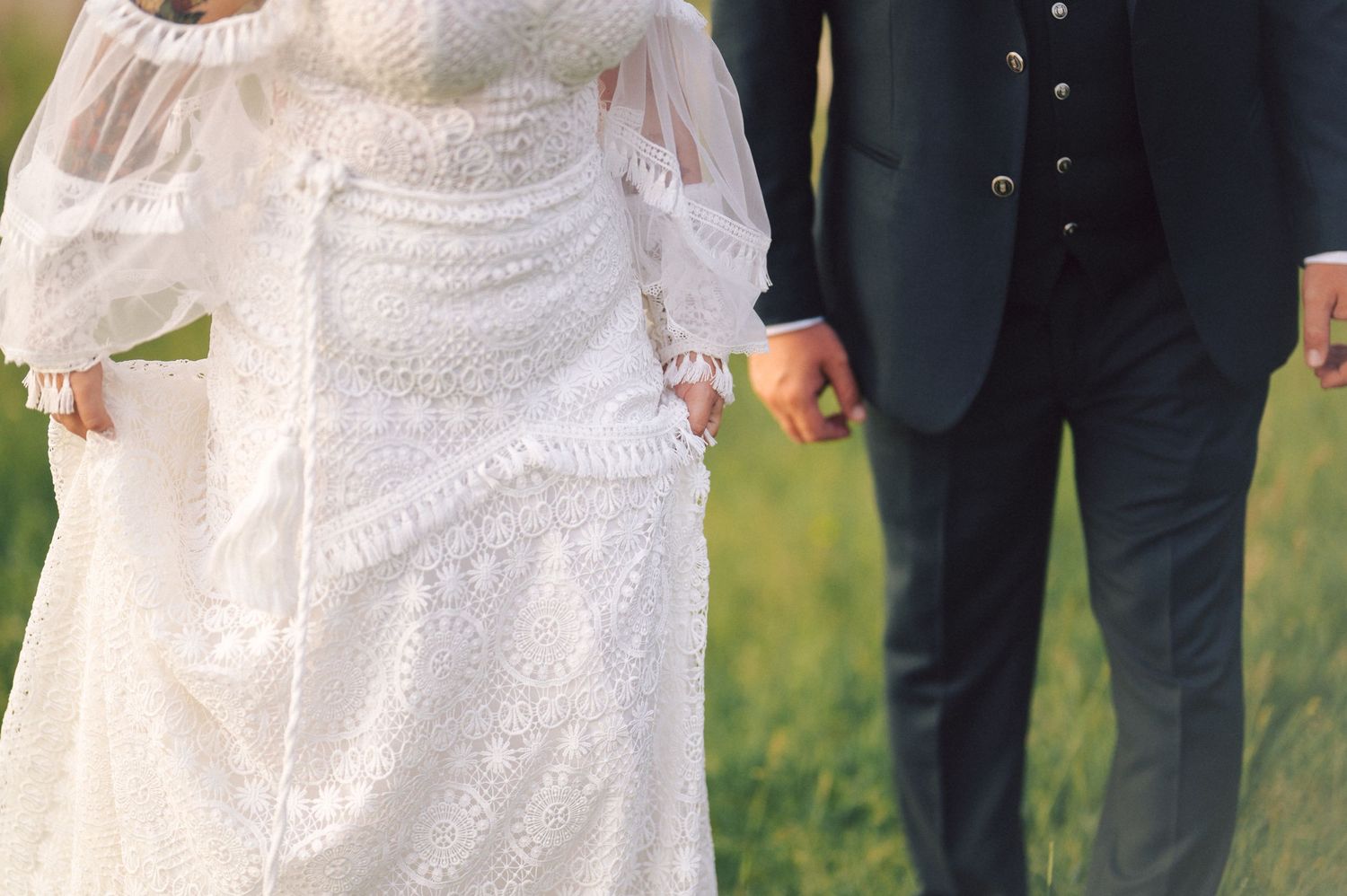 Wedding party members in formal attire pose outdoors on a grassy lawn in a line formation.