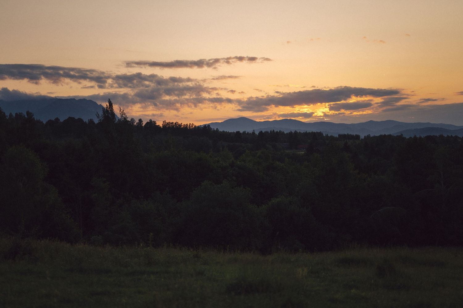Panoramic sunset over distant mountains with dramatic orange clouds streaking across the darkening evening sky.