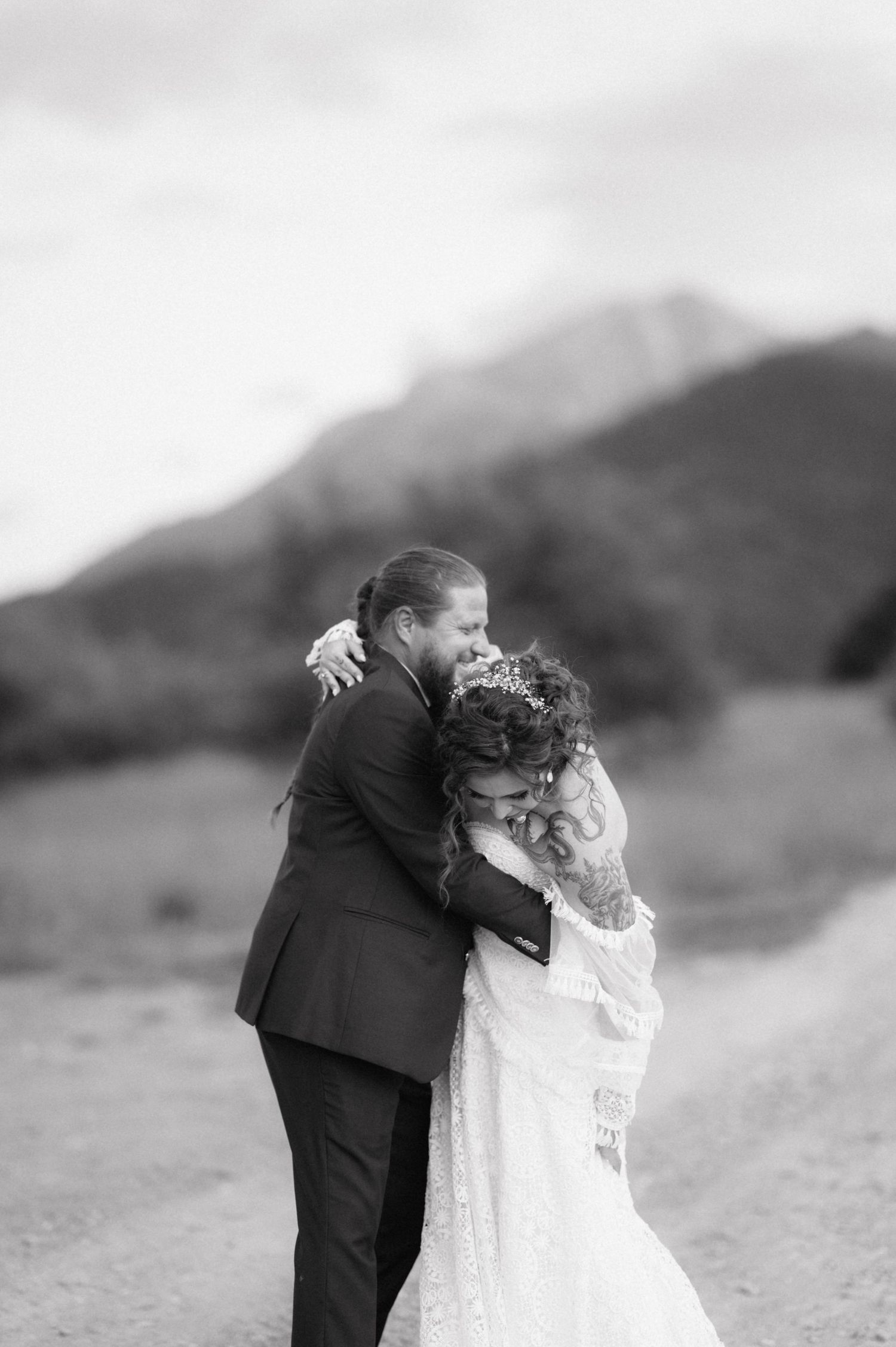 A newlywed couple share a sweet moment in a field with mountains in the background.