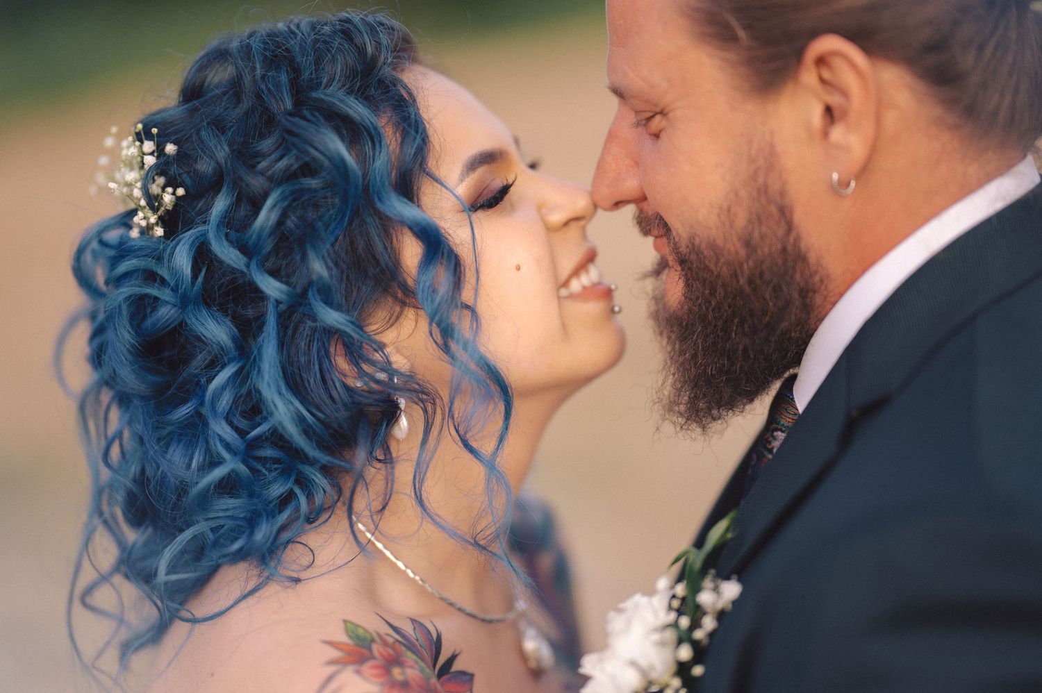 A tender romantic moment between newlyweds as they stand close, with one wearing vibrant blue curled hair and a sparkly hair accessory.