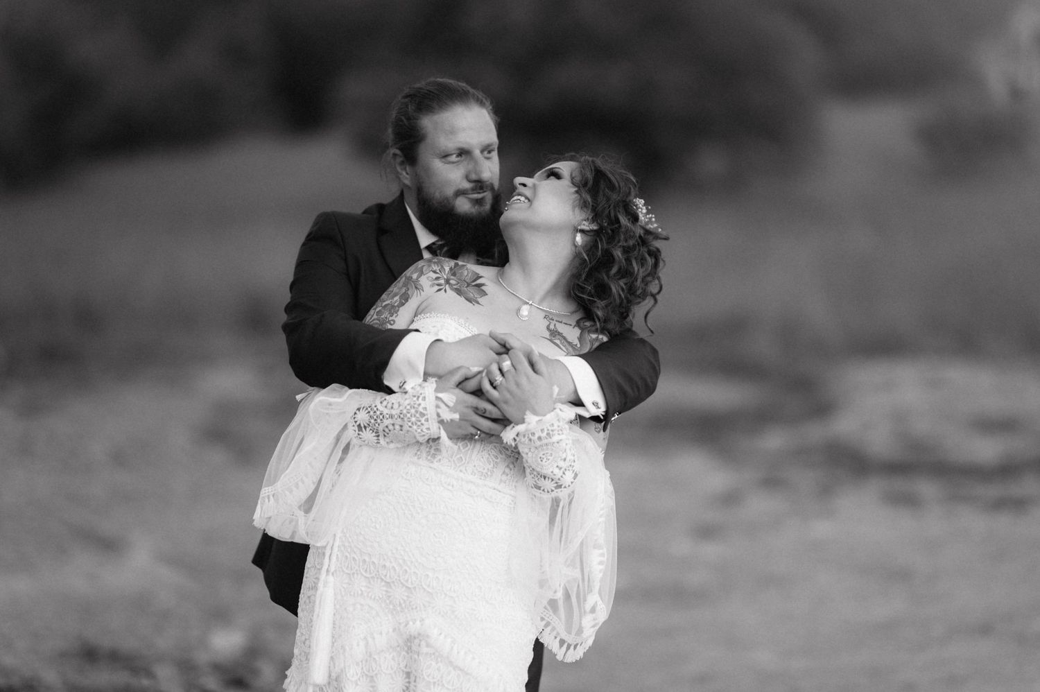 A romantic black and white wedding photo captures an intimate moment between newlyweds outside in soft lighting.