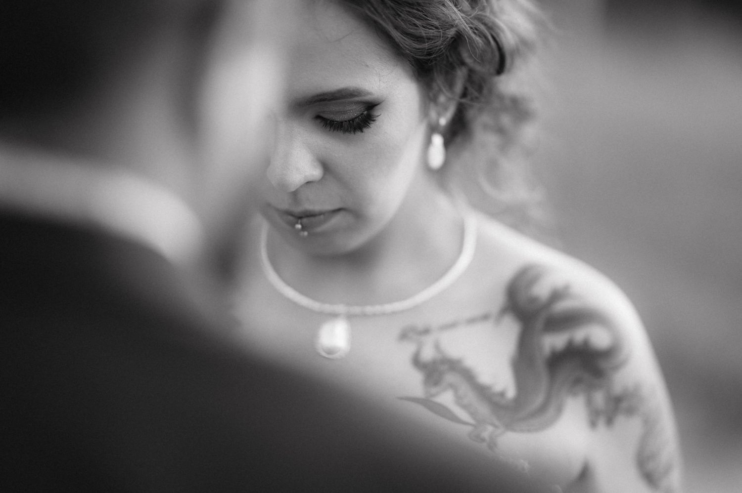 A soft black and white artistic wedding photograph captures close-up profile detail with delicate jewelry.