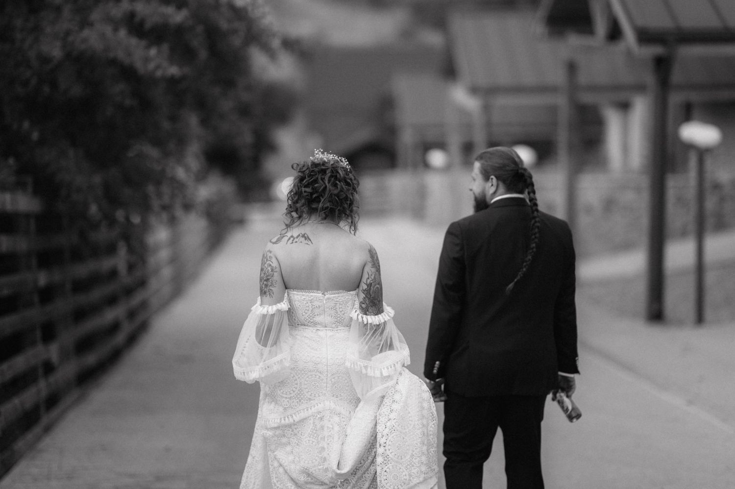 A romantic black and white photo of a bride and groom walking away together on a city street.