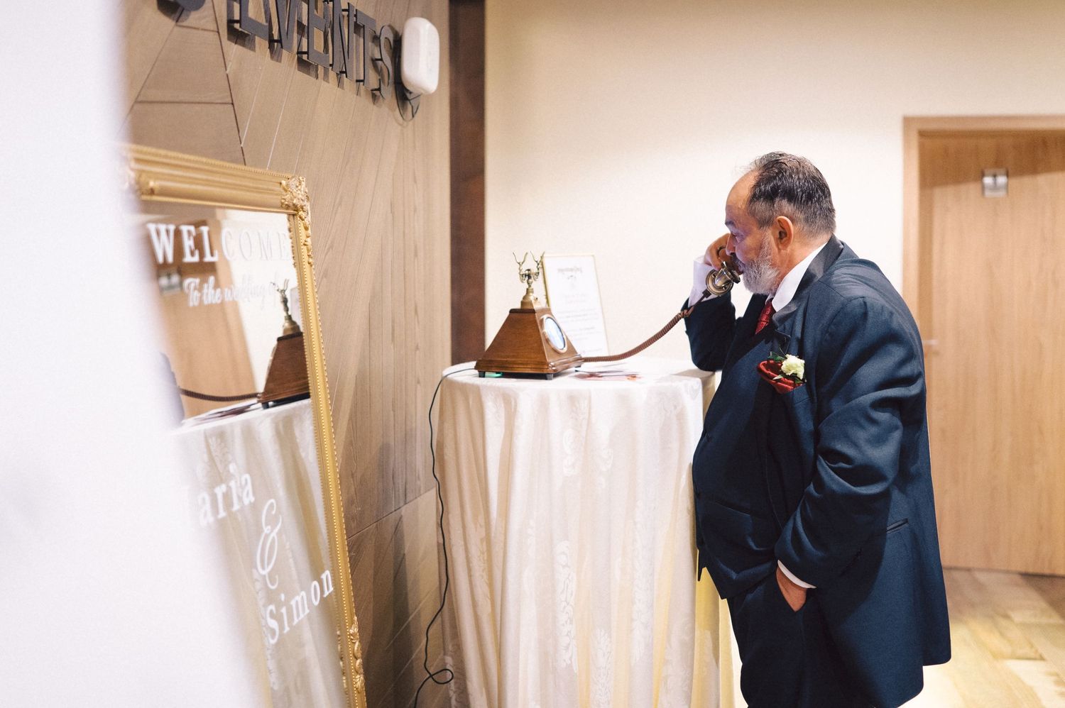Two people in business suits use a retro telephone at a wooden desk with hanging pendant lamps in an office setting.