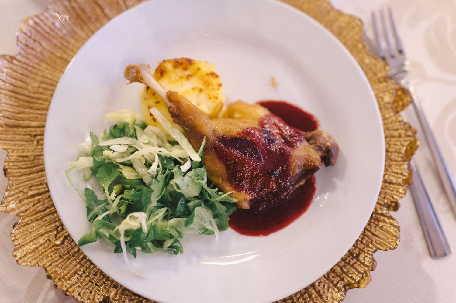 Elegant plated dinner featuring roasted duck with red wine sauce, fresh salad, and golden potato gratin on white china.