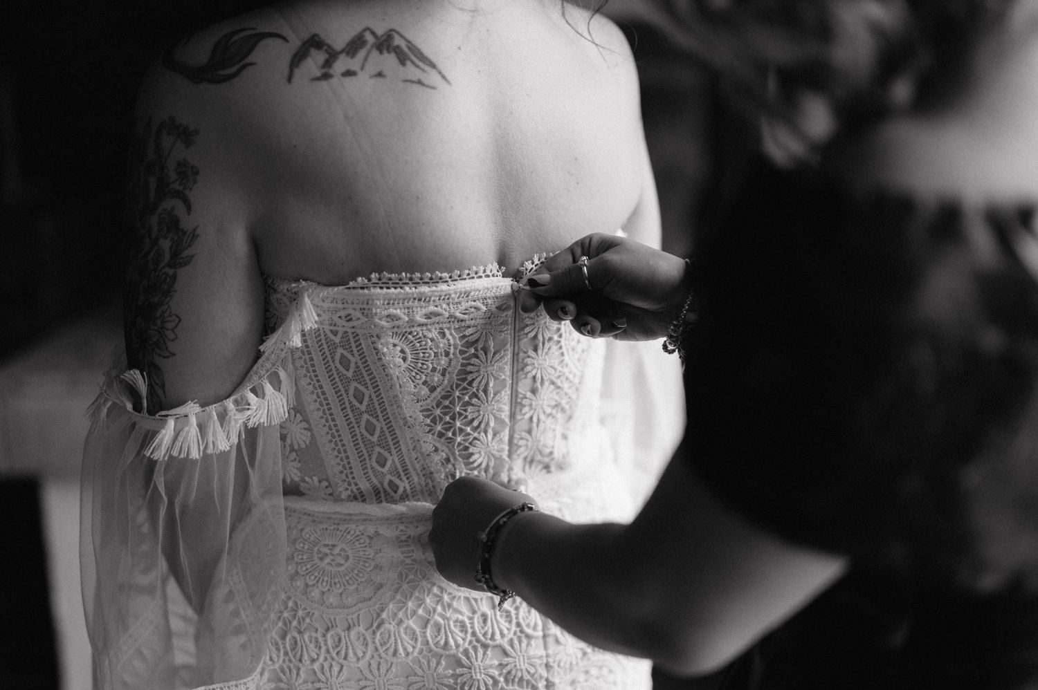 Black and white closeup photo of hands lacing up the back of an ornate white lace corset.