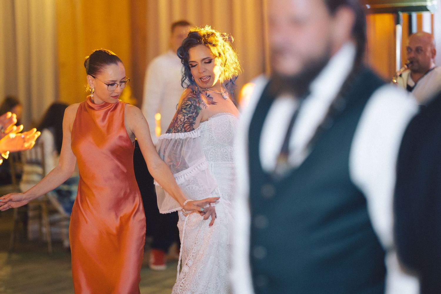 A party scene with attendees dancing and celebrating at a wedding reception with warm lighting.