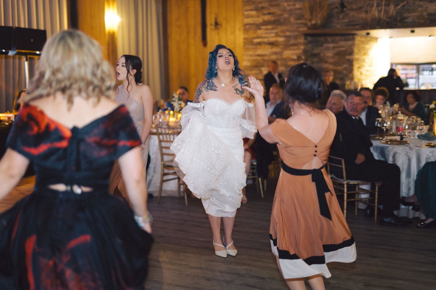 Guests dancing and celebrating at a rustic barn wedding reception under warm ambient lighting.