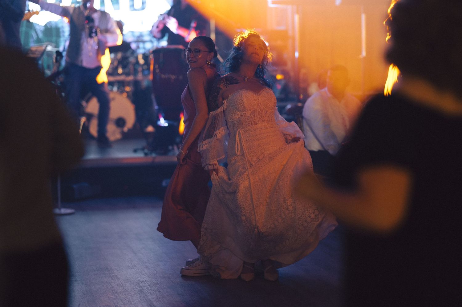 People dance in traditional dress at a dimly lit venue with orange lighting and silhouetted figures on a dance floor.