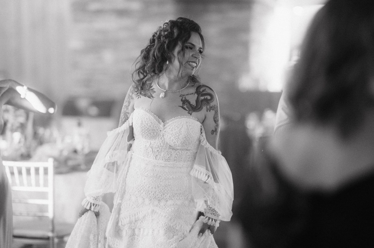 Black and white photograph of a bride dancing and smiling during a wedding celebration at an outdoor reception.