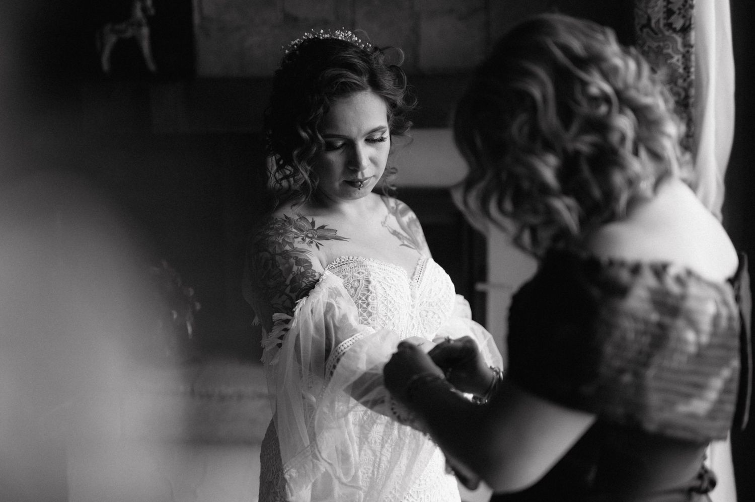 A bride stands in front of a mirror in a black and white photograph while getting ready for her wedding ceremony.