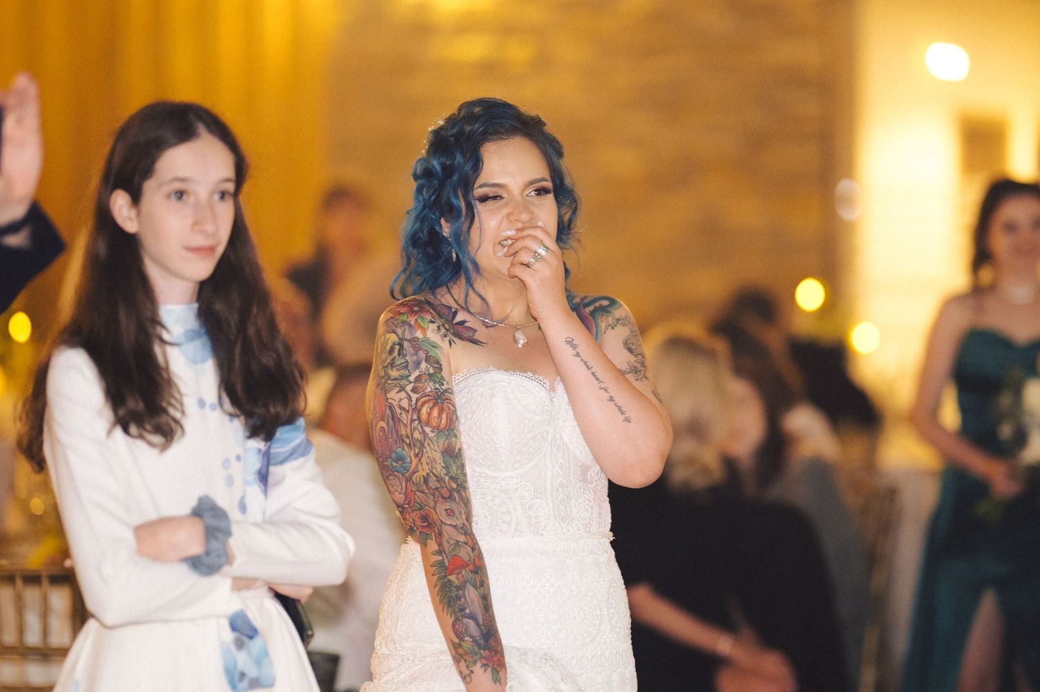 Wedding reception guests dance and celebrate in an elegantly lit ballroom with golden lighting and festive atmosphere.