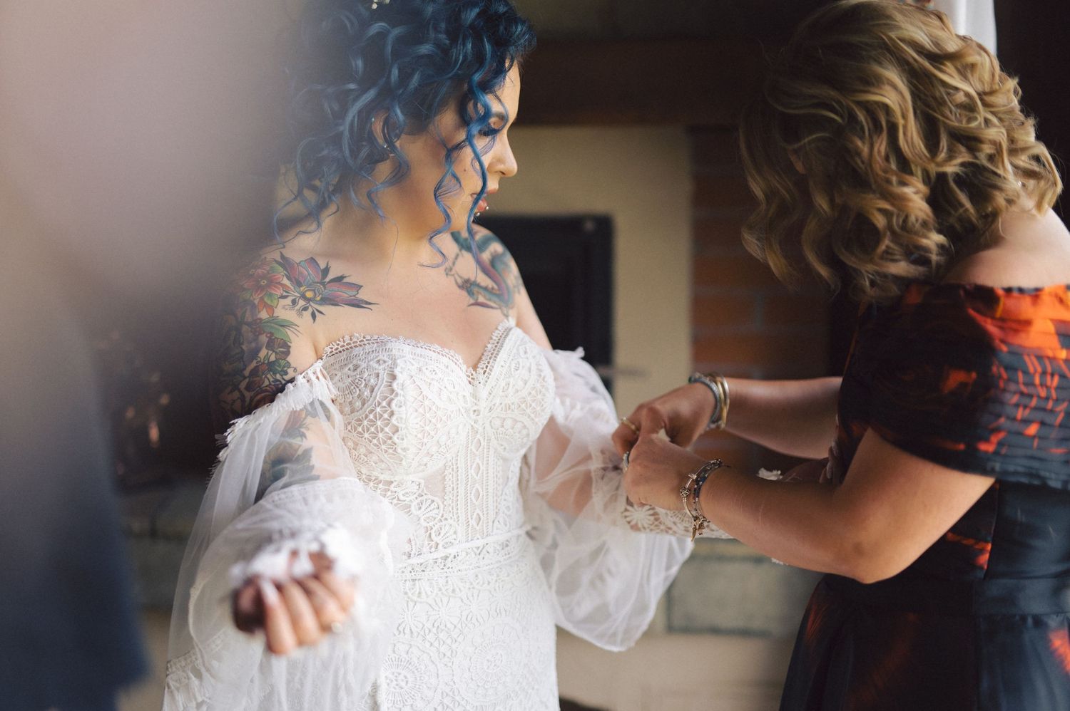 A bride in an elegant white lace wedding dress gets help with final preparations before her ceremony.