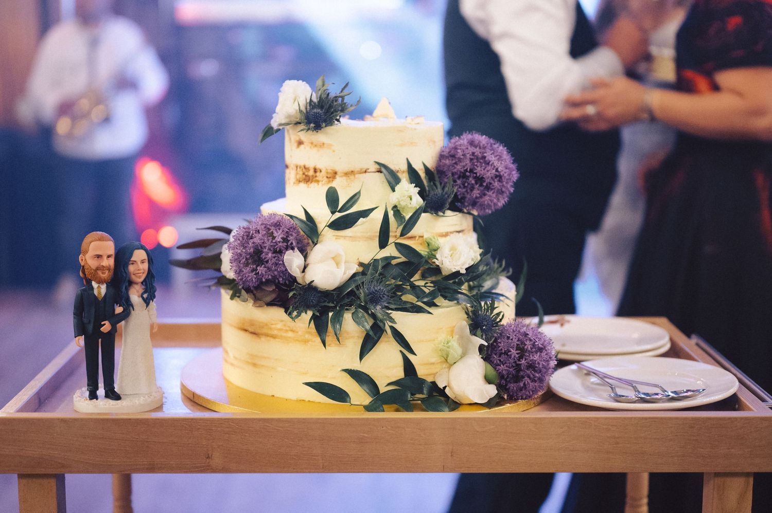Close up views of a yellow and purple floral wedding cake decorated with fresh flowers being served at a reception.