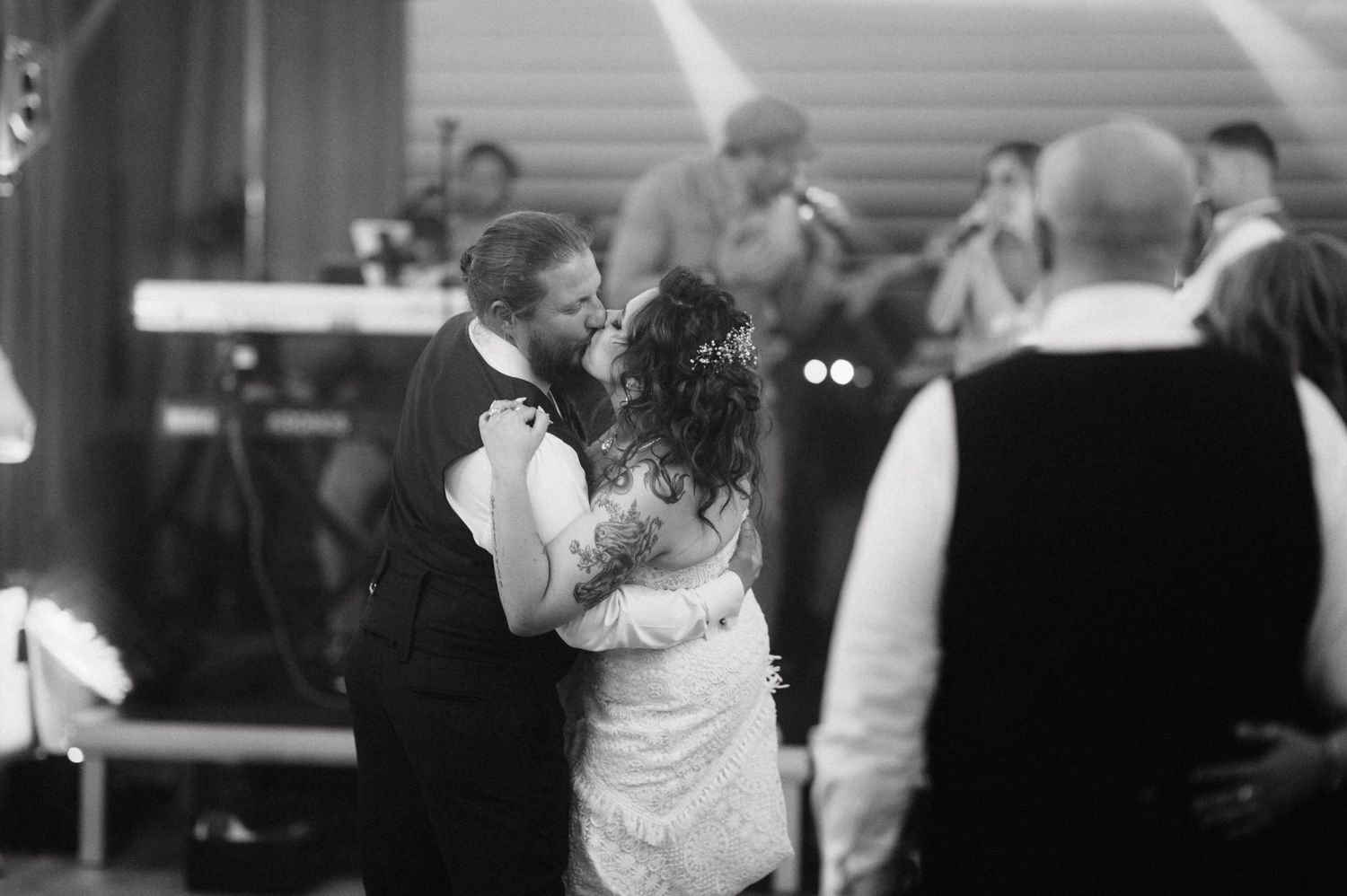A couple shares a romantic dance together at a reception while other guests mingle in the background.
