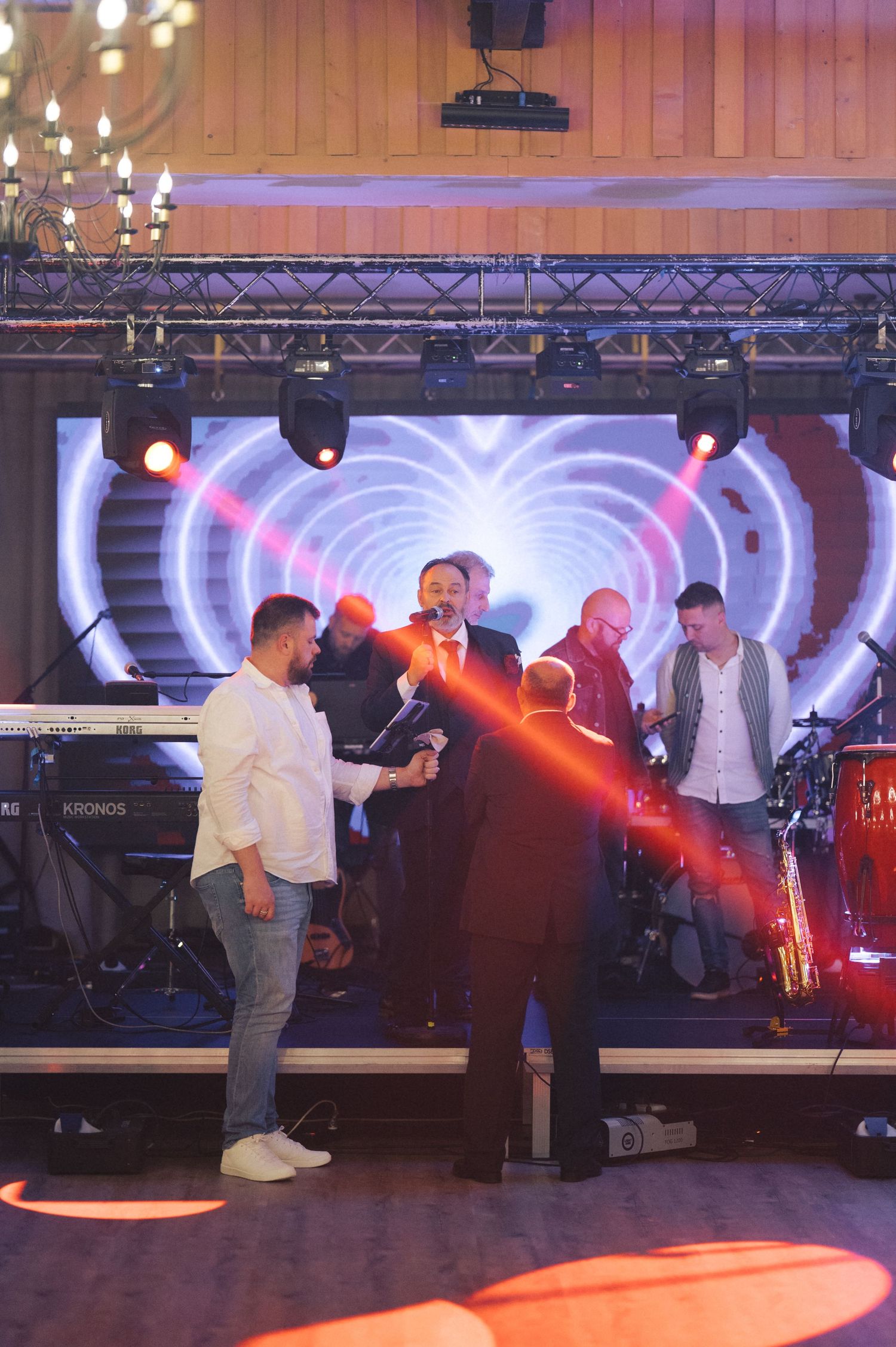 A performer on stage with band members during a live concert with colorful lighting and stage equipment.
