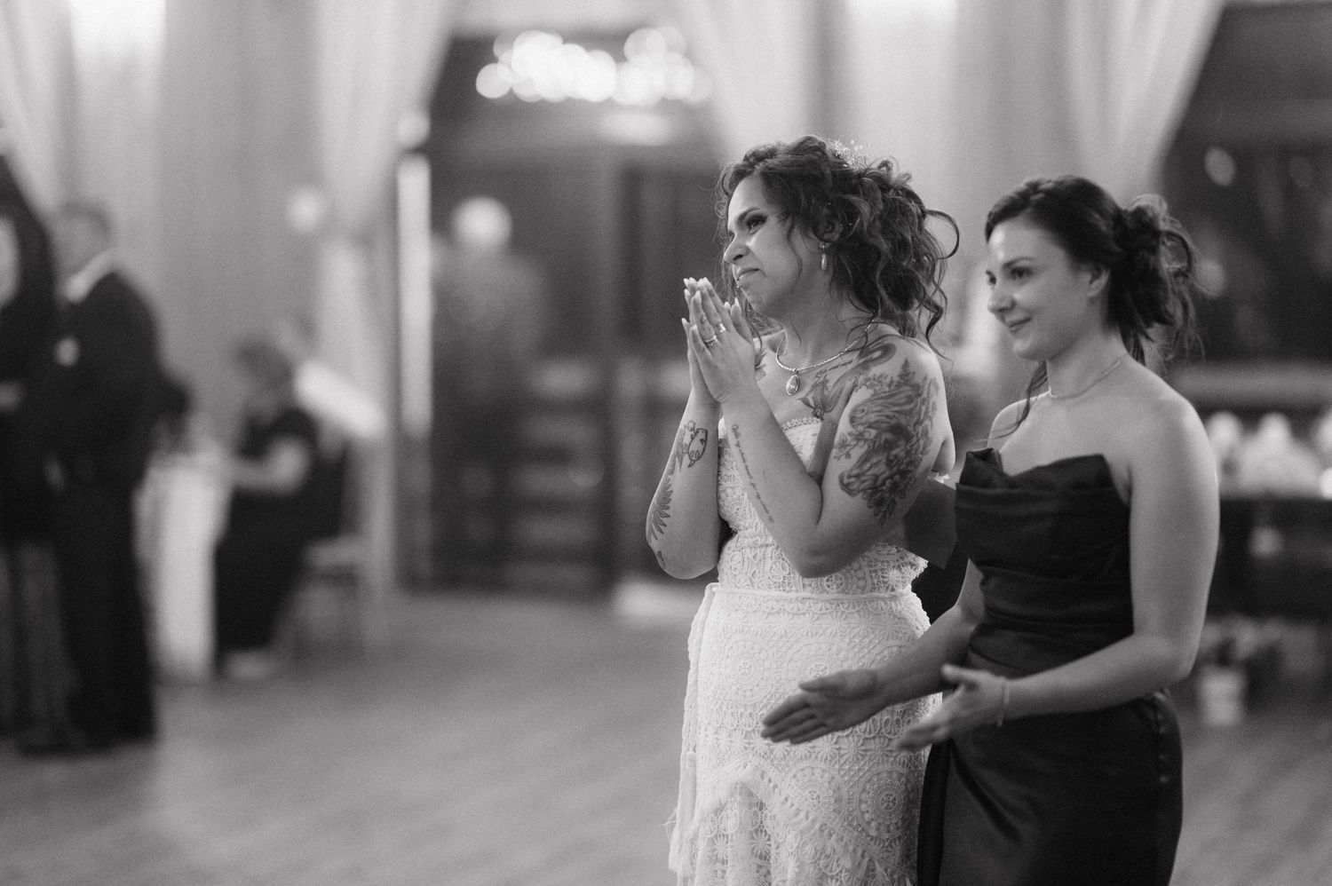 Two women sharing an emotional moment on the dance floor at an elegant indoor reception venue captured in black and white.