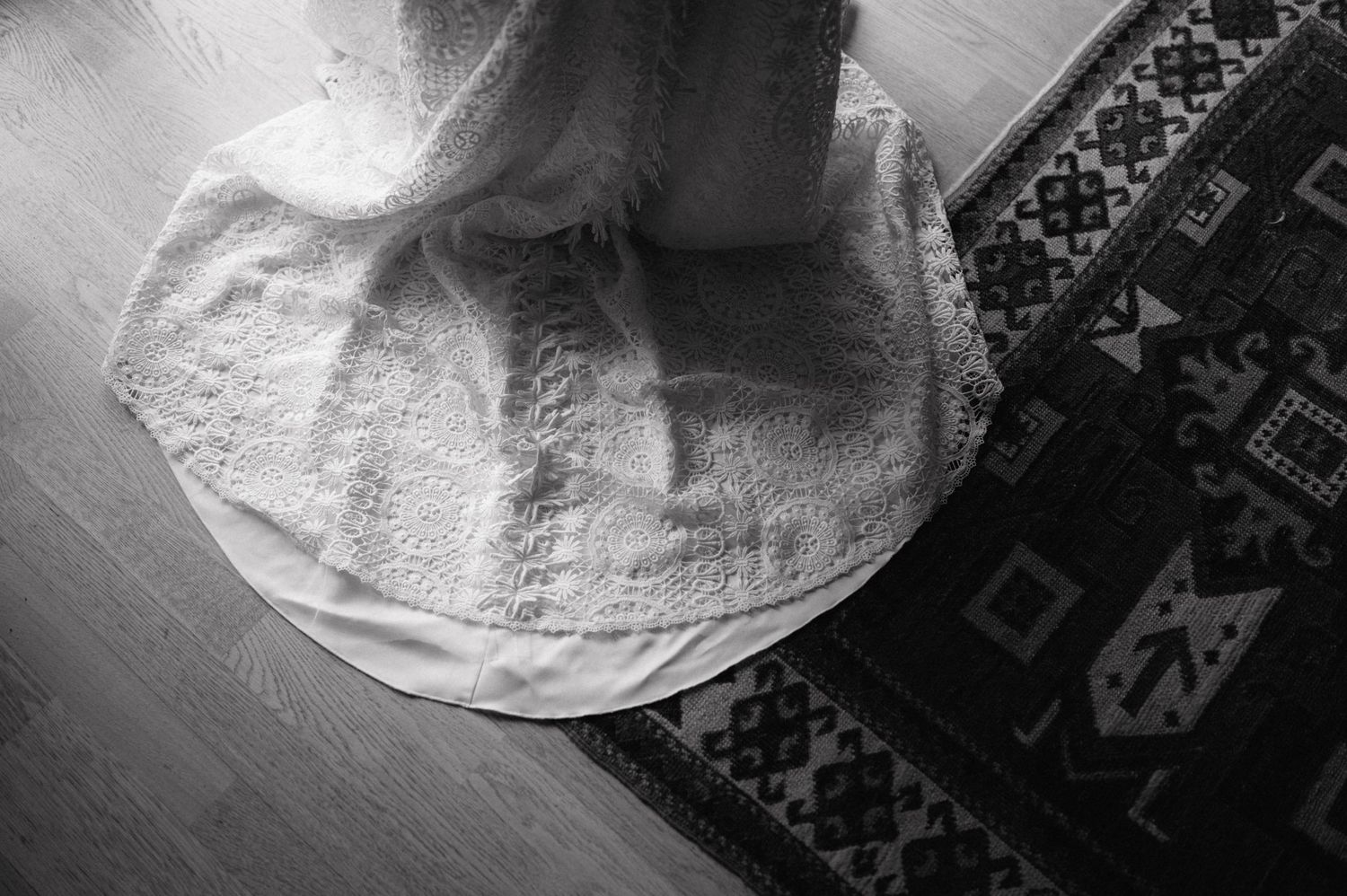 Black and white photograph showing a round white cloth on a dark patterned rug viewed from above.