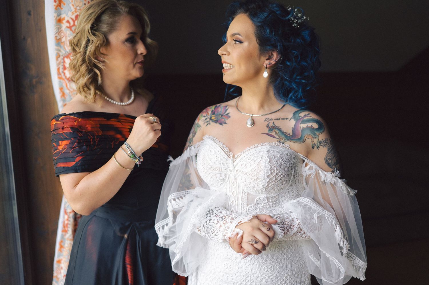 Two people in bridal attire dance elegantly in a dark room with dramatic side lighting.