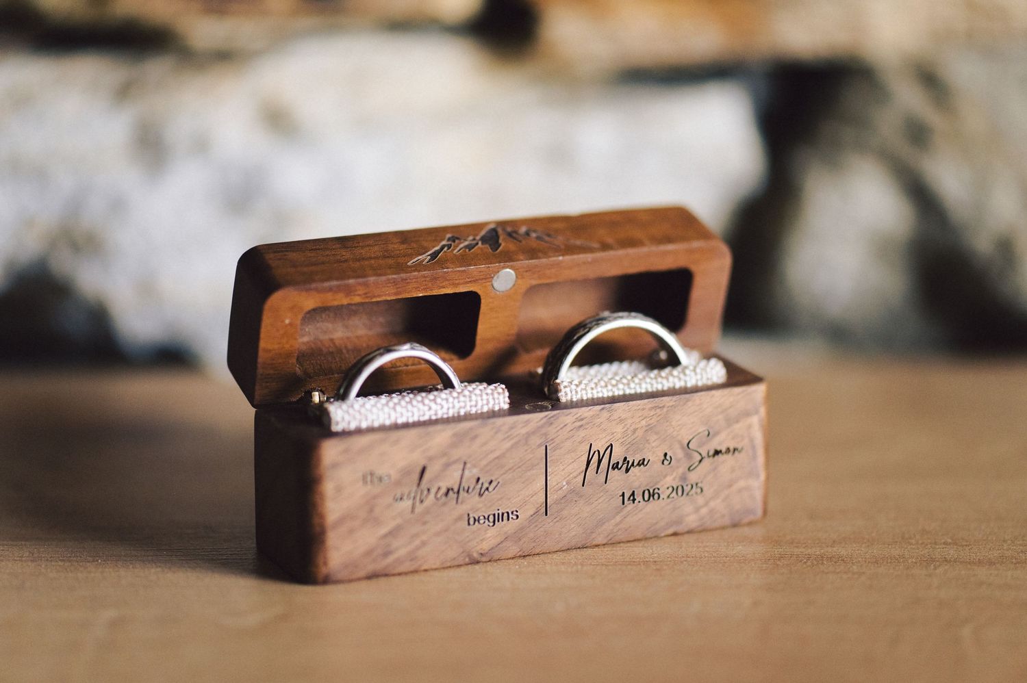 Wedding rings nestled in a small wooden box with engraved text on a wooden surface.
