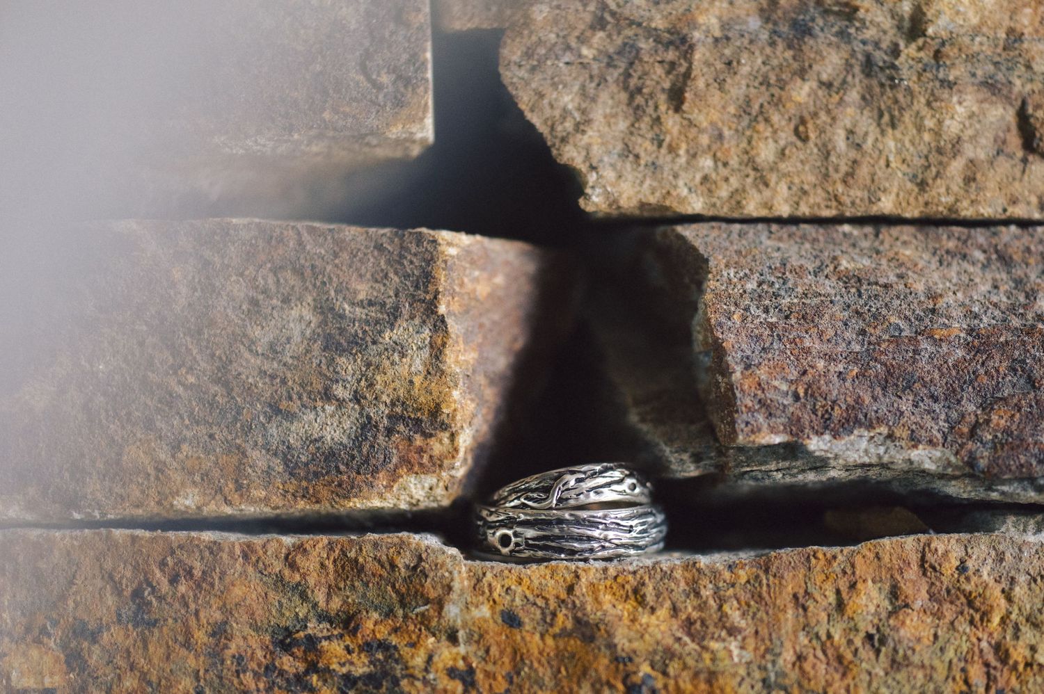 Close-up of a rustic metal ring against textured stone blocks with dramatic shadowing.