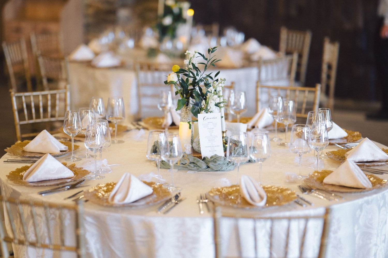 White table linens with gold charger plates and champagne napkins create an elegant wedding reception table setting.