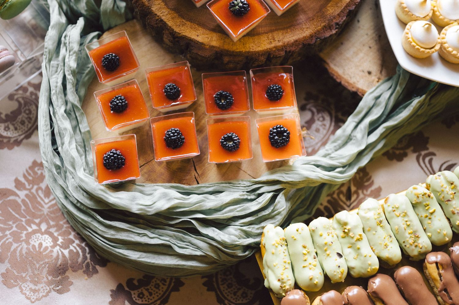 Elegant dessert platter featuring orange jelly squares with berries and white cookies arranged on decorative serving plates.