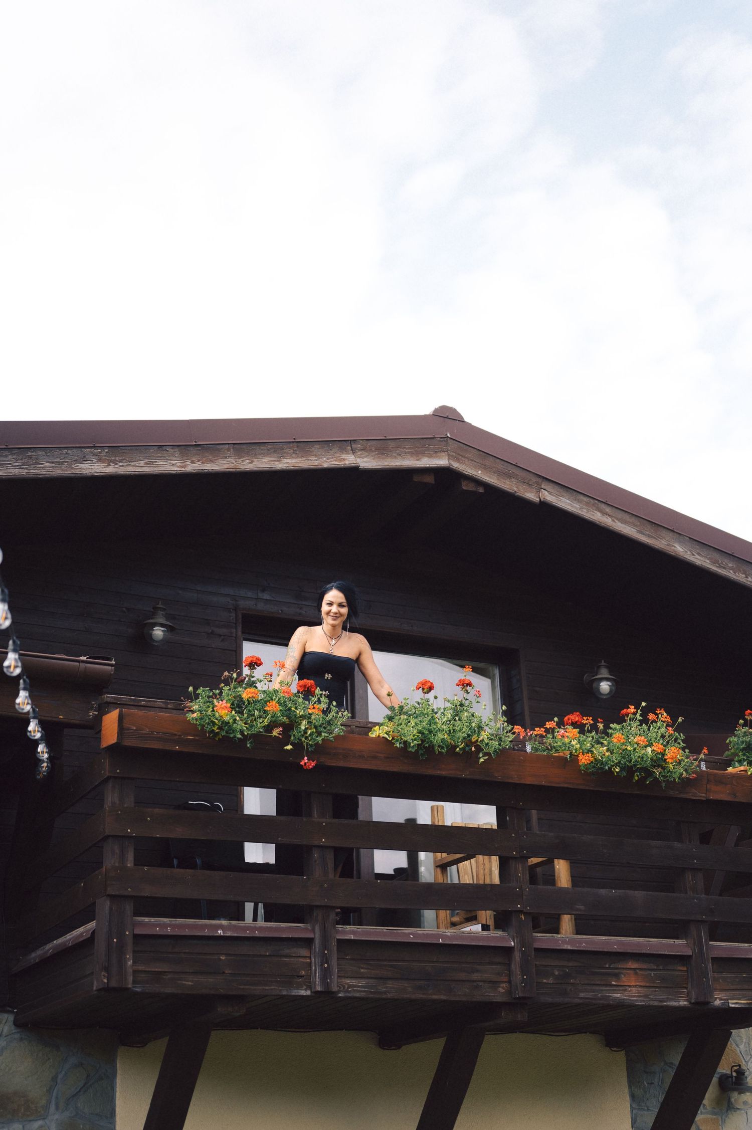 Rustic wooden balcony decorated with colorful flowers in planters on mountain lodge railing.