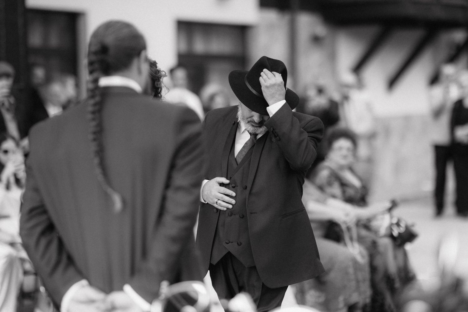A vintage black and white photo shows someone covering their face with their hand while standing near others outdoors.