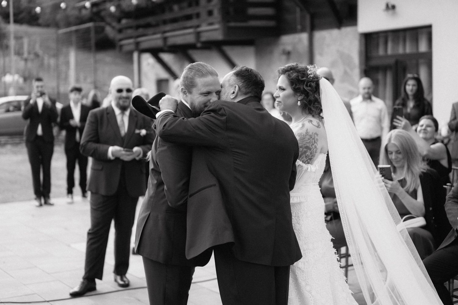 Black and white wedding photo showing an emotional moment between wedding party members at an outdoor celebration.