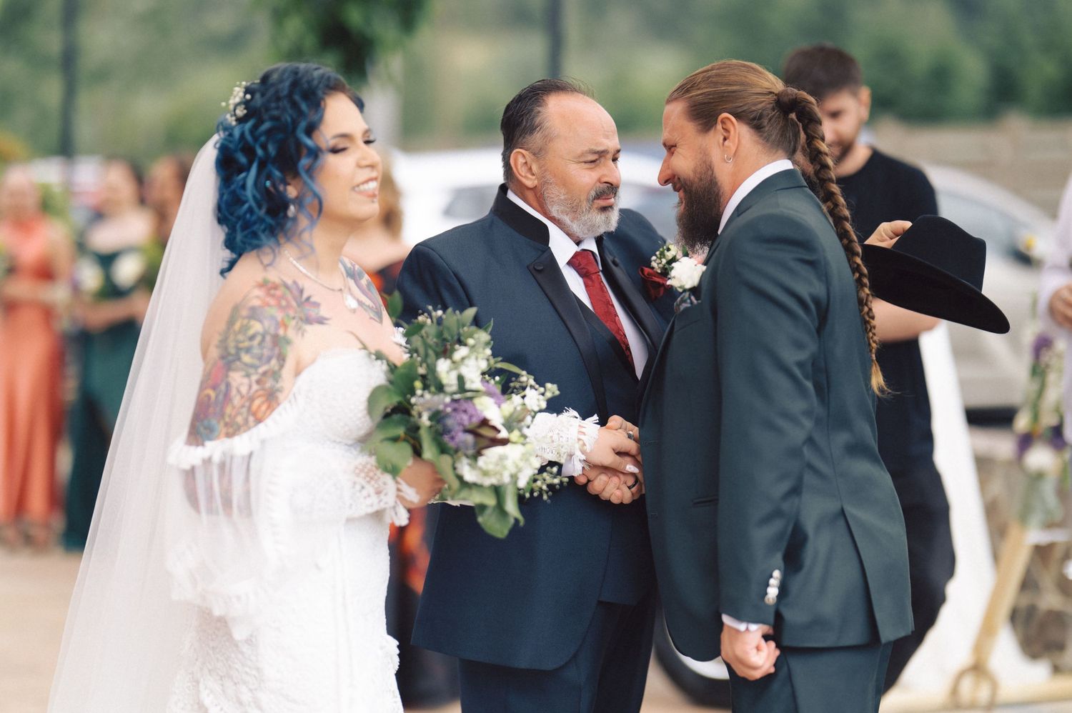 An outdoor wedding ceremony taking place with figures in formal attire and a white floral bouquet.