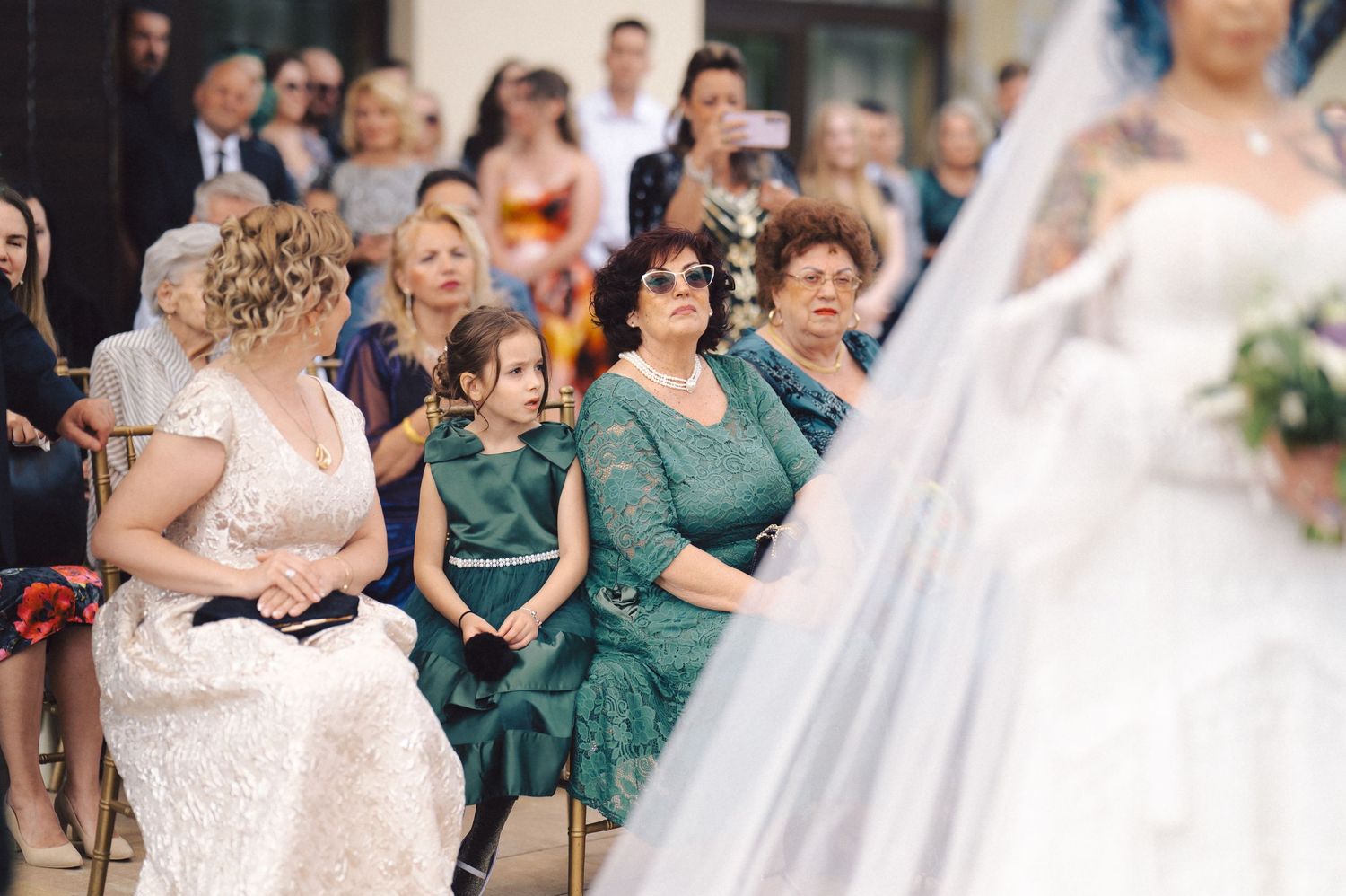 Wedding ceremony attendees seated in green dresses watching the celebration.