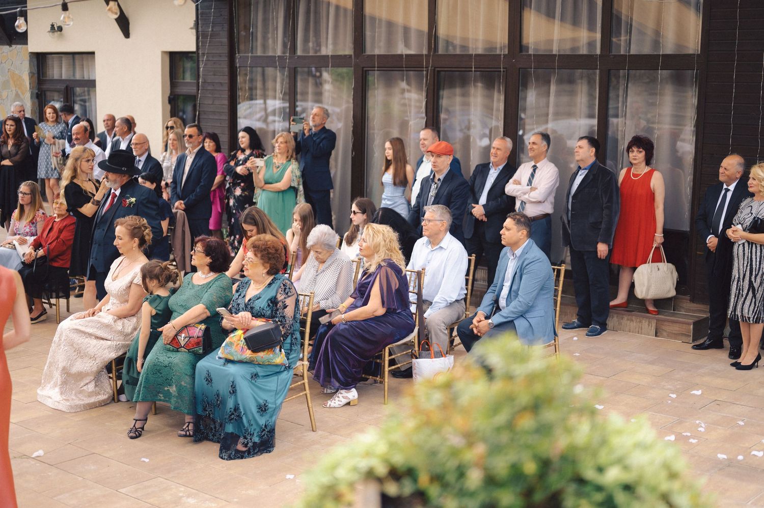 A wedding ceremony with guests gathered outdoors standing in front of a building entrance while confetti fills the air.