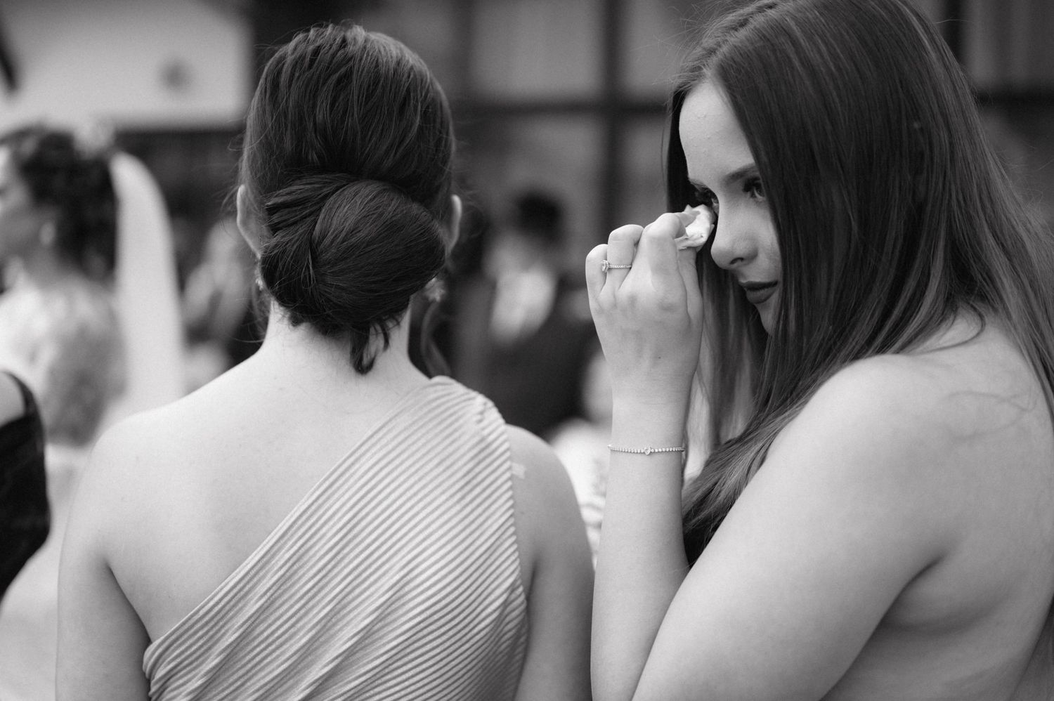 Black and white candid photo of two people at an event, one wiping their eye while another faces away.