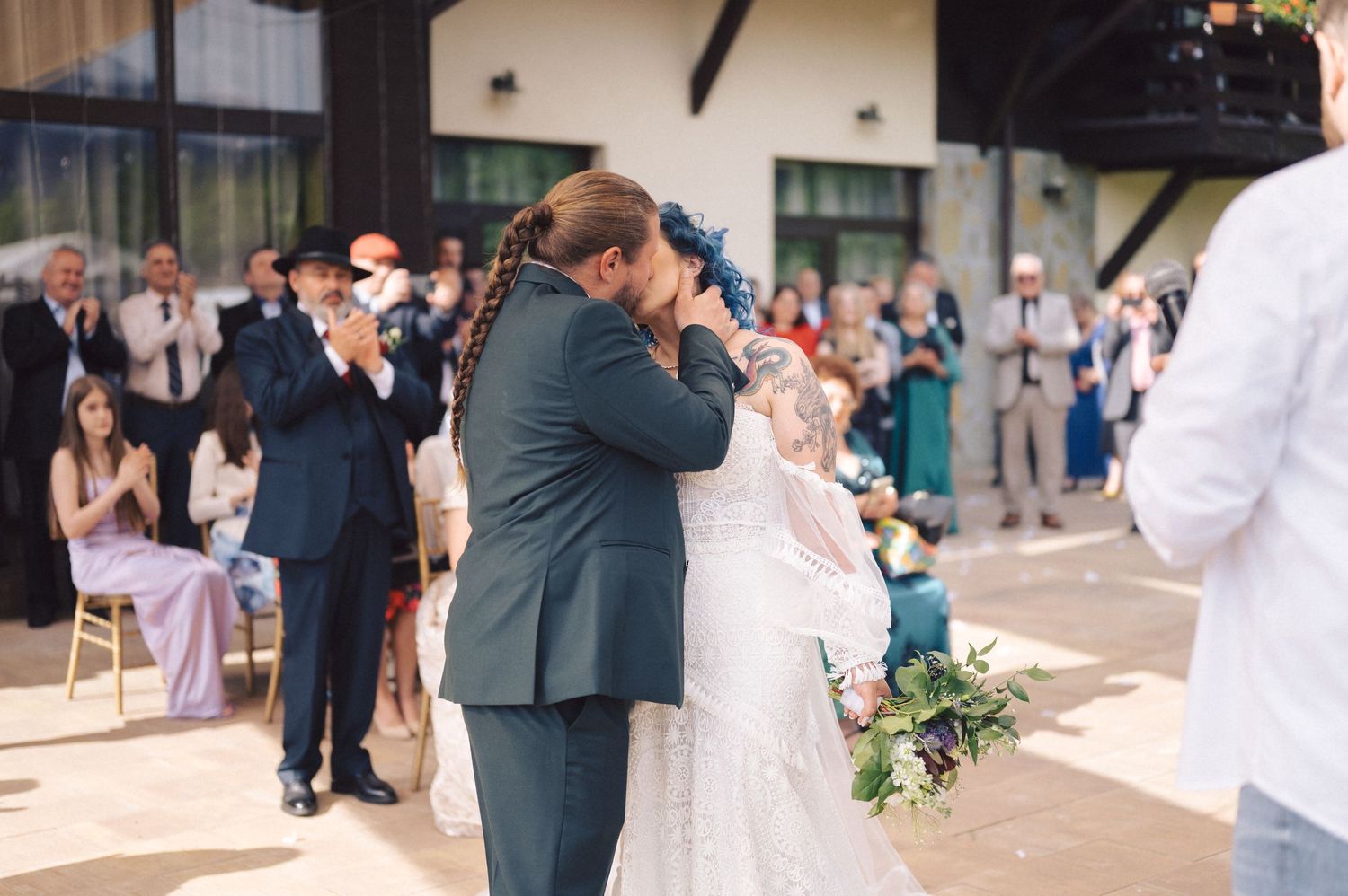 A tender embrace is shared between two people during a wedding ceremony as guests look on at an outdoor venue.