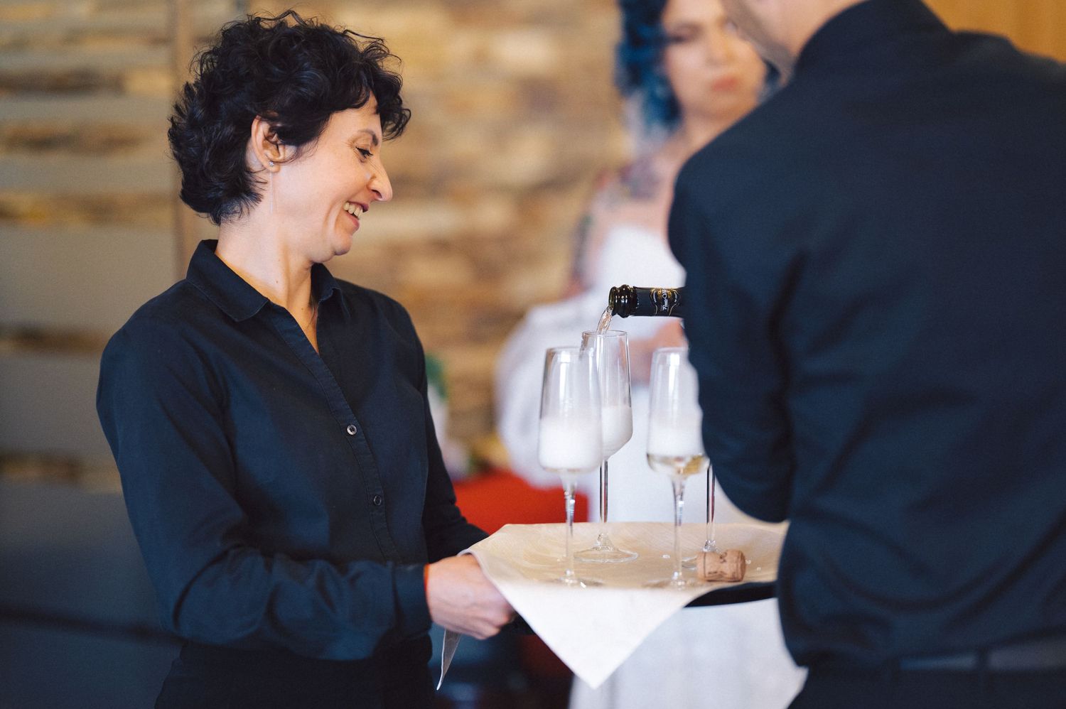 Restaurant servers in dark uniforms carrying wine glasses and dishes while working in dining establishment.