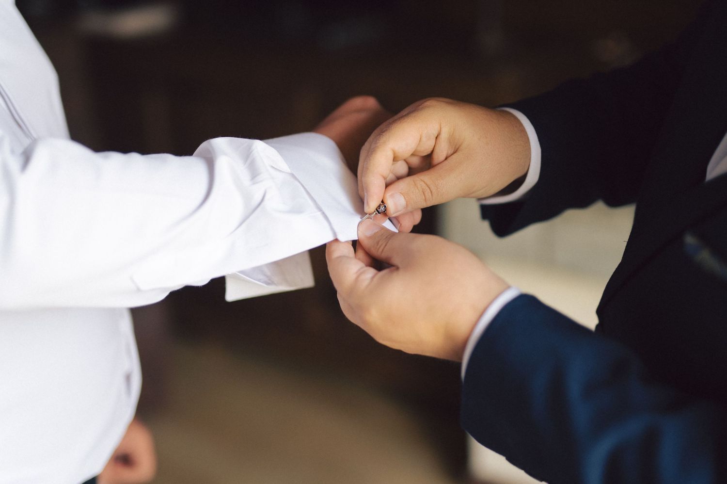 Close-up shot of hands adjusting formal white dress shirt cuffs during wedding preparations.