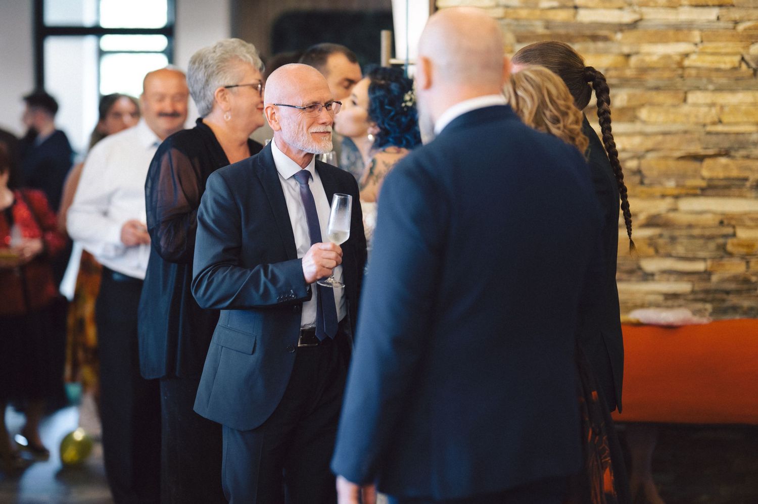 Guests in formal business attire socialize at a networking event with stone wall decor in the background.