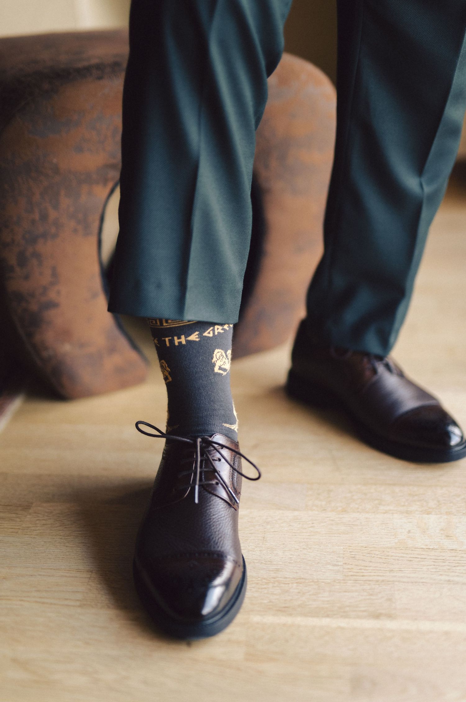 Stylish black dress shoes paired with blue suit pants and novelty printed socks on wooden floor.